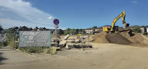 Baustelle mit Bagger, Erdhaufen und einem itComes-Videoturm-Banner am Bauzaun.
