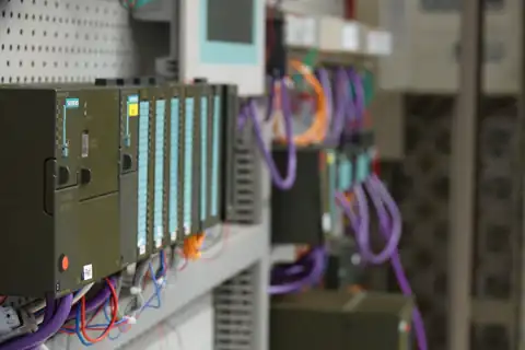 Reihe grüner Steuerungsbaugruppen mit angeschlossenen Leitungen in einem Schaltschrank.