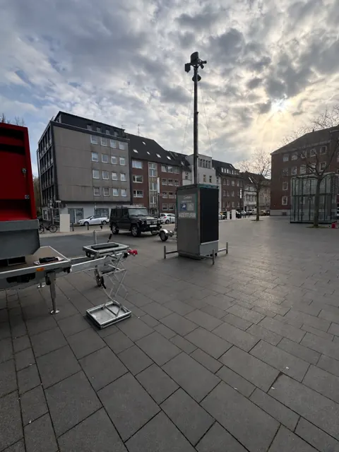 Mobiler Videoturm mit ausgefahrenem Mast auf einem Platz vor Gebäuden.